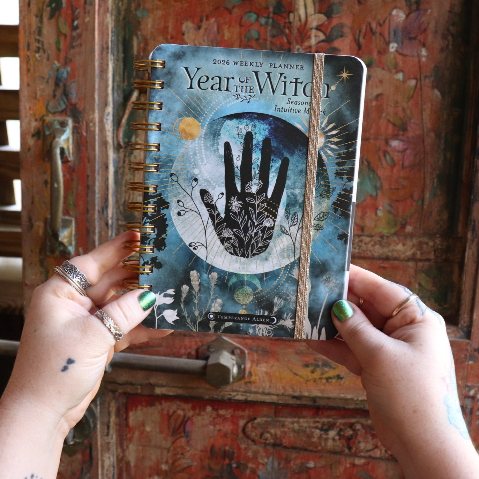 Someone holding the Year of the Witch 2026 Weekly Planner in front of a door.
