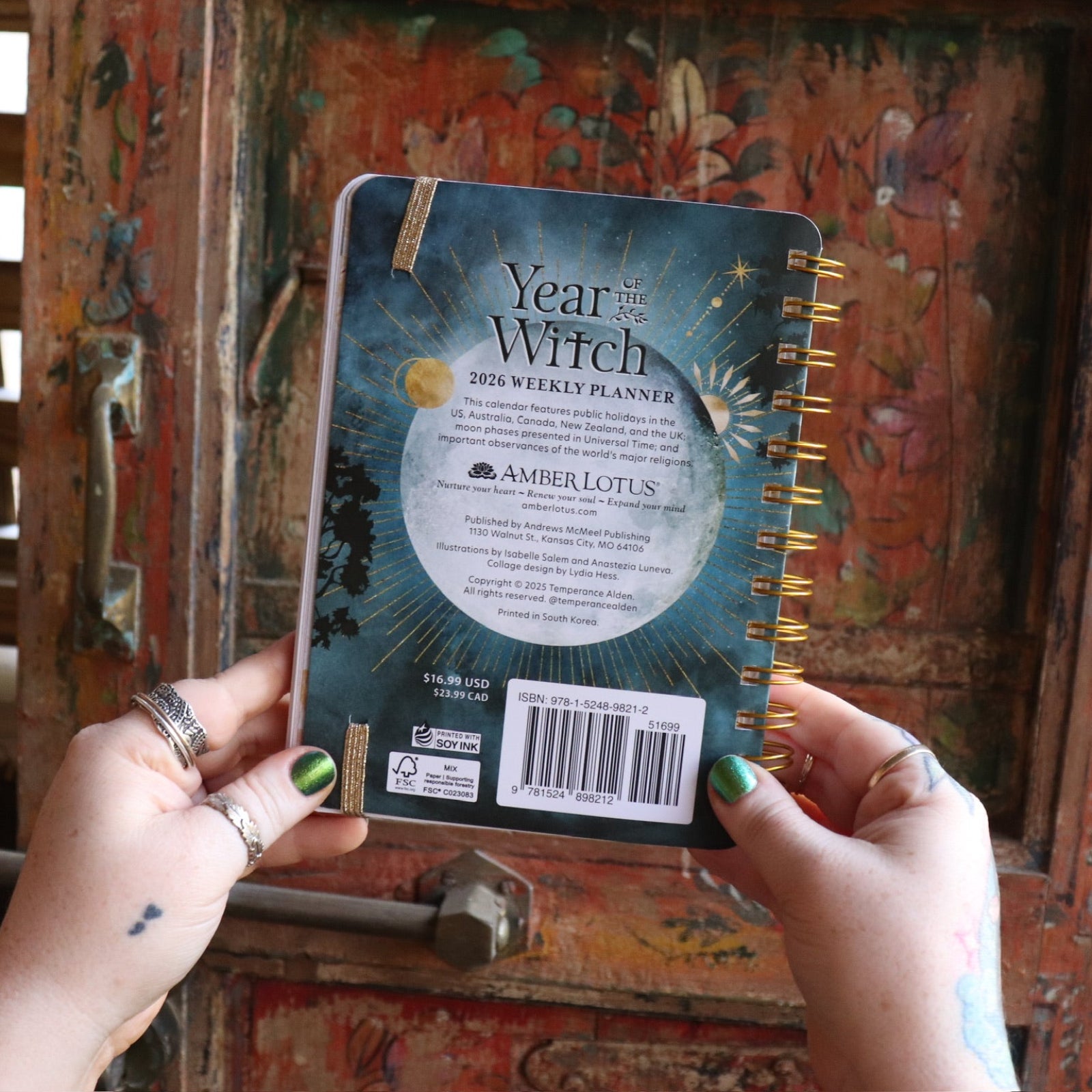Someone holding the Year of the Witch 2026 Weekly Planner in front of a door, showing off the back.