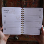 Someone holding the Year of the Witch 2026 Weekly Planner in front of a door, showing off the pages.