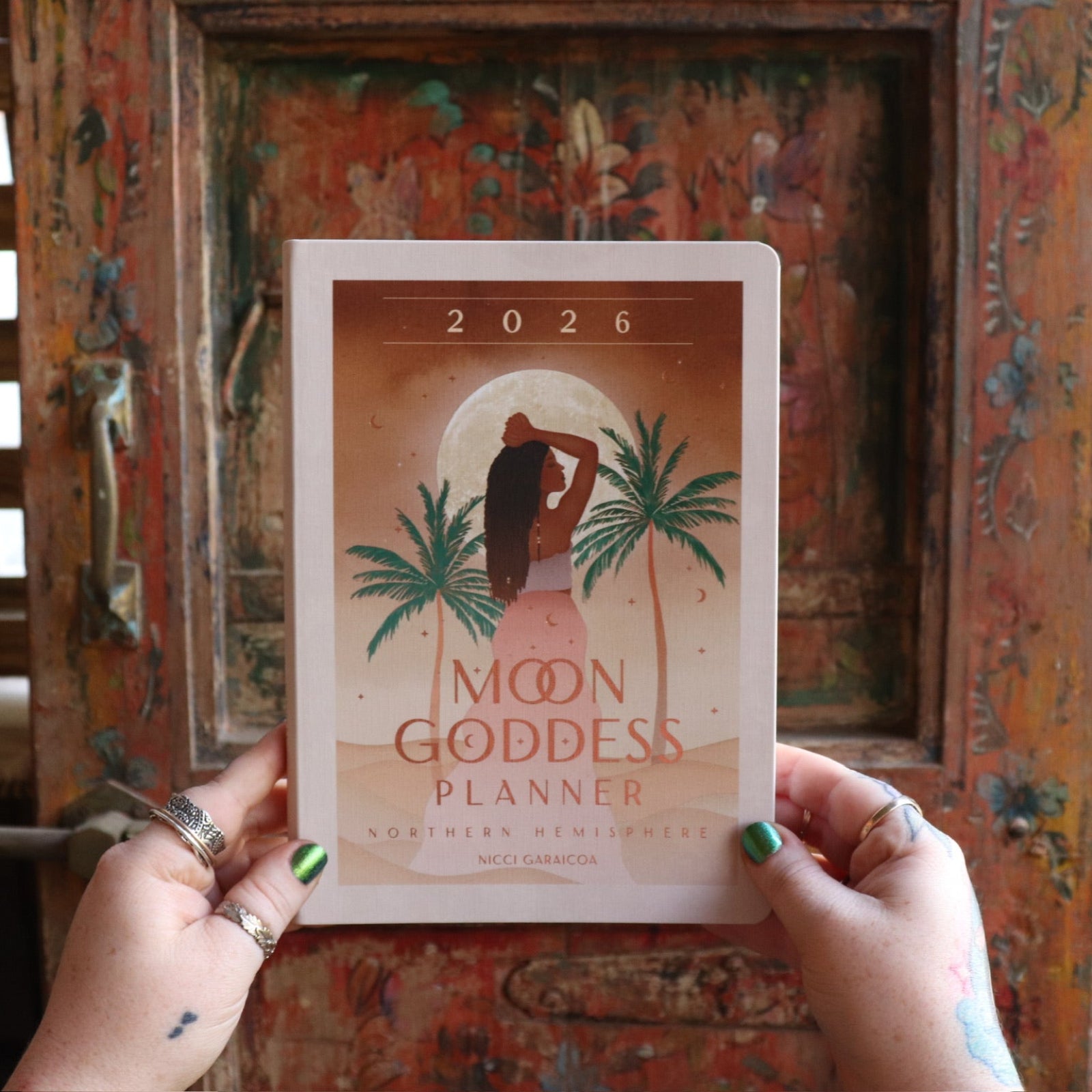 Someone holding the 2026 Moon Goddess Northern Hemisphere Planner Calendar in front of a wooden door.