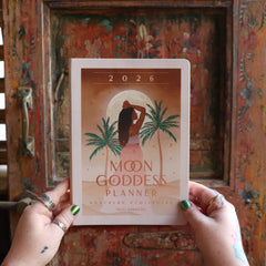 Someone holding the 2026 Moon Goddess Northern Hemisphere Planner Calendar in front of a wooden door.
