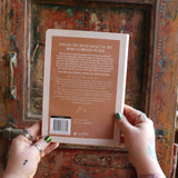 Someone holding the 2026 Moon Goddess Northern Hemisphere Planner Calendar in front of a wooden door, showing off the back.