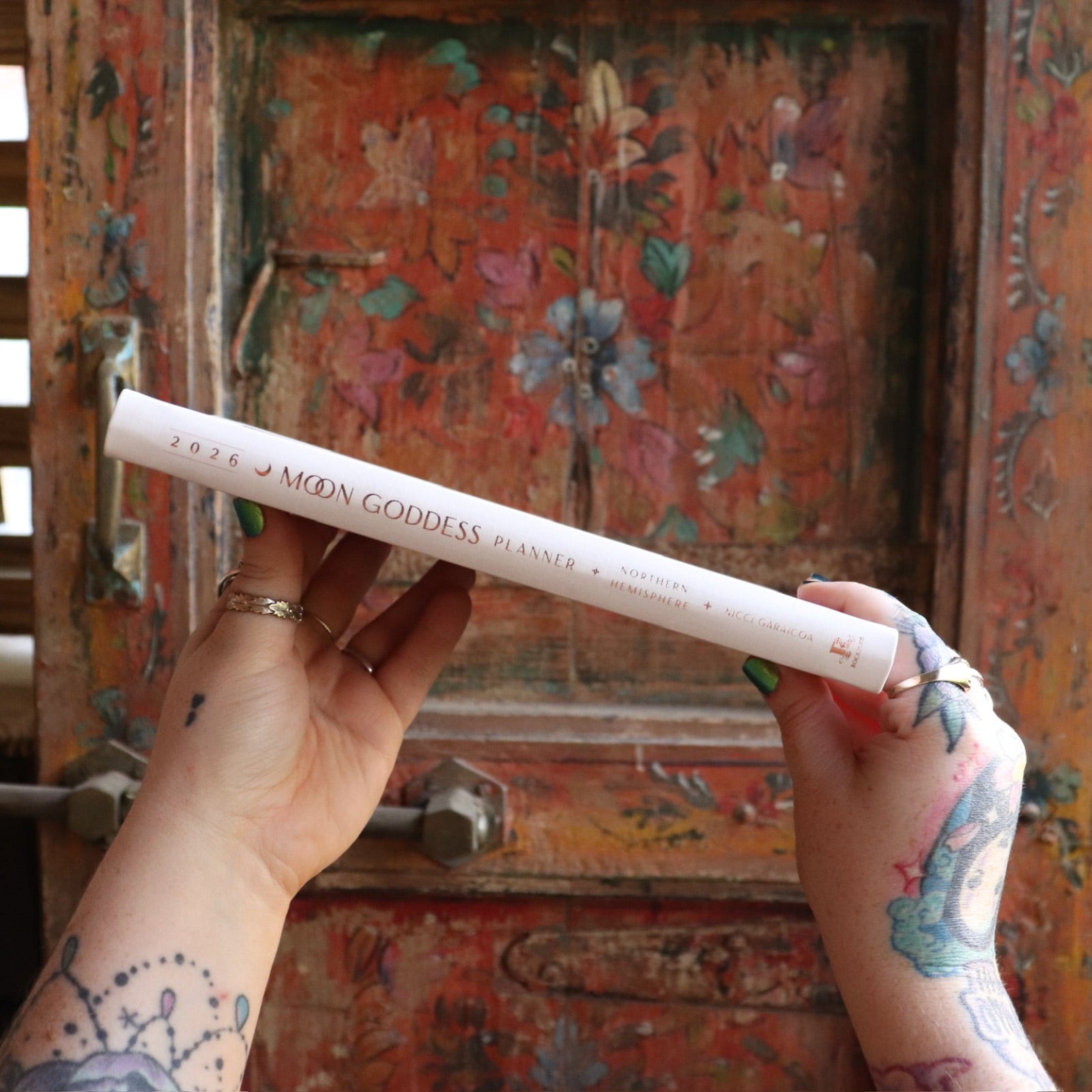 Someone holding the 2026 Moon Goddess Northern Hemisphere Planner Calendar in front of a wooden door, showing off the side.
