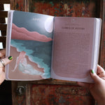 Someone holding the 2026 Moon Goddess Northern Hemisphere Planner Calendar in front of a wooden door, showing off the pages.