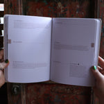 Someone holding the 2026 Moon Goddess Northern Hemisphere Planner Calendar in front of a wooden door, showing off the pages.