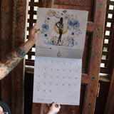 Someone holding up the Year of the Witch 2026 Wall Calendar, showing off the pages.