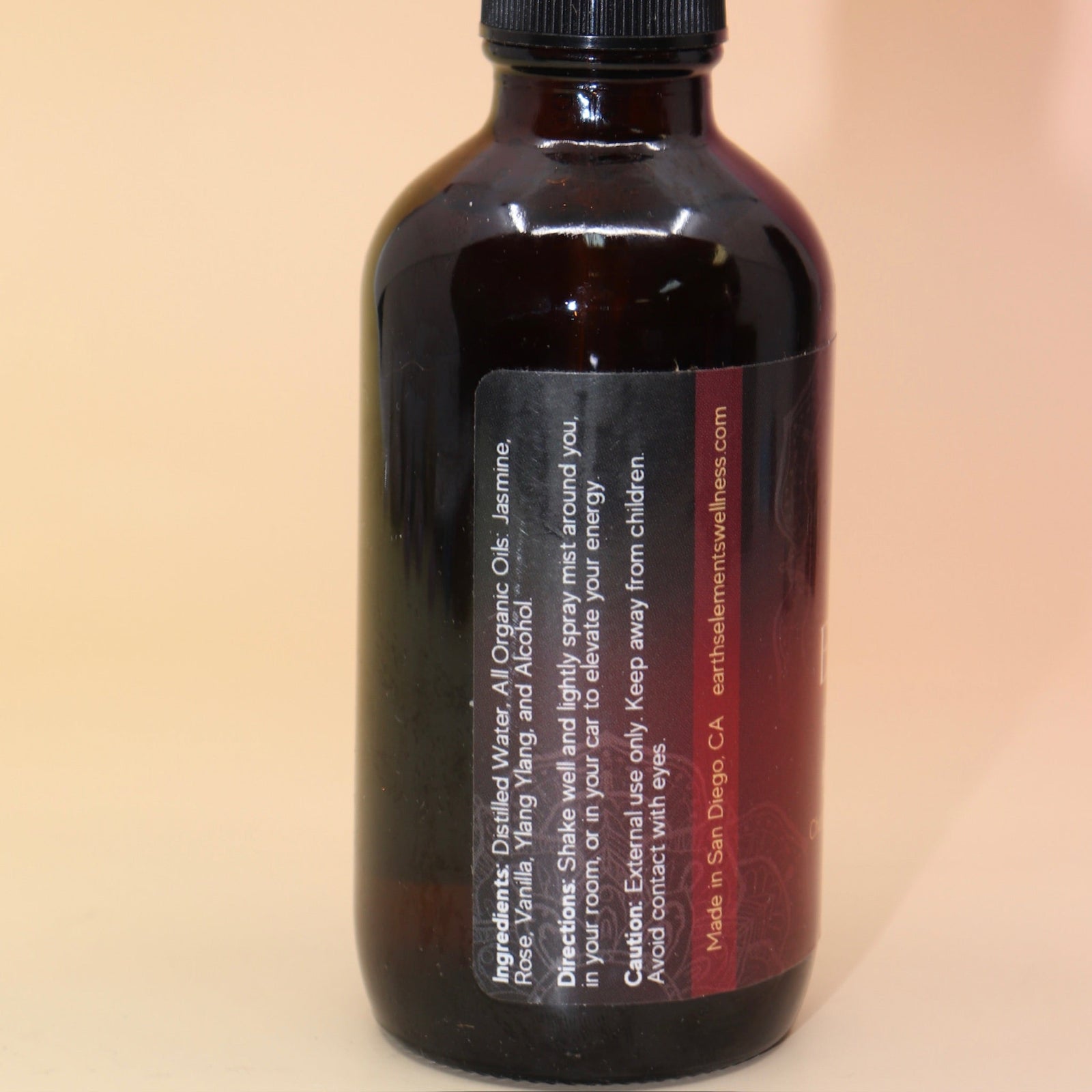 The Love Essence Organic Crystal Charged Energy Spray on a pink and yellow background, showing off the side.