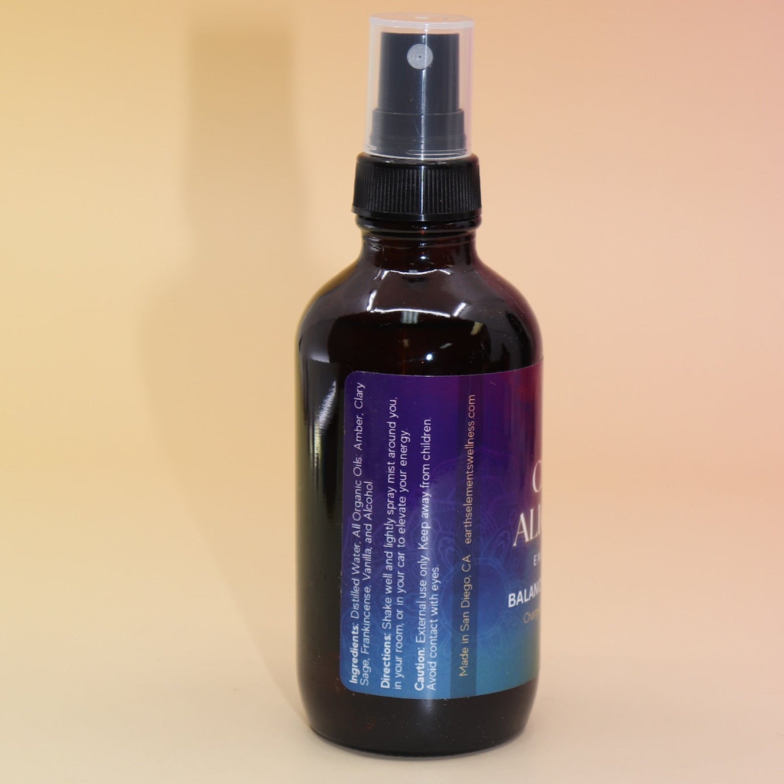 The Chakra Alignment Organic Crystal Charged Energy Spray on a pink and yellow background, showing off the side.
