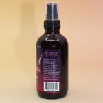 The Angel Protection Organic Crystal Charged Energy Spray on a pink and yellow background, showing off the side.