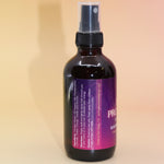The Angel Protection Organic Crystal Charged Energy Spray on a pink and yellow background, showing off the side.