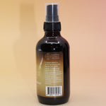 The Infinite Abundance Organic Crystal Charged Energy Spray on a pink and yellow background, showing off the side.