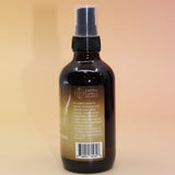 The Infinite Abundance Organic Crystal Charged Energy Spray on a pink and yellow background, showing off the side.