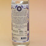 An up-close image of the back of the White Sage Spiritual Cleansing Water 7.5 oz on a pink and yellow background.