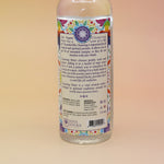 An up-close image of the back of the 7 Chakras Spiritual Cleansing Water 7.5 oz on a pink and yellow background. 