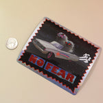 The No Fear Glitter Sticker next to a coin against a crystal on a pink and yellow background. 