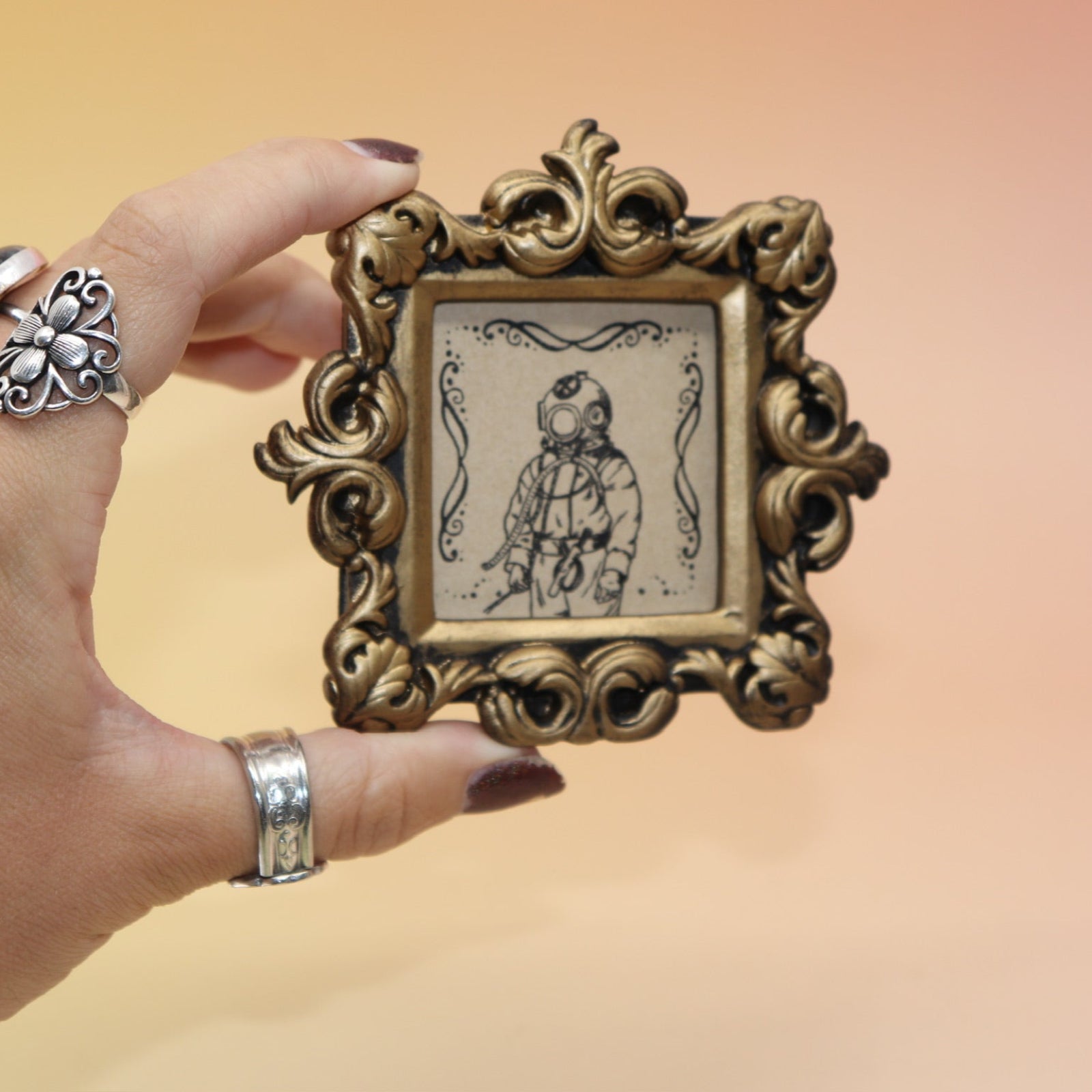 Someone holding the Deep Sea Diver Mini Vintage Framed Print in front of a pink and yellow background.