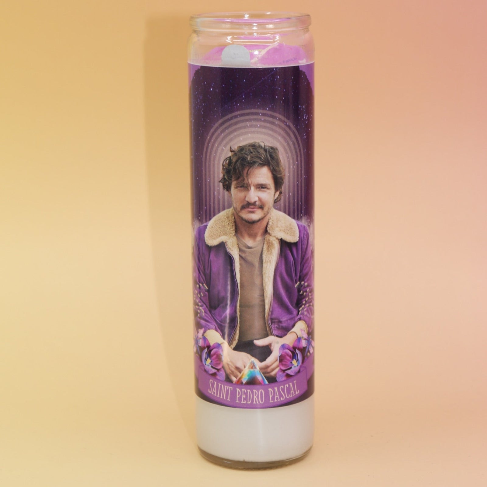 The Pedro Pascal Devotional Prayer Candle on a pink and yellow background.
