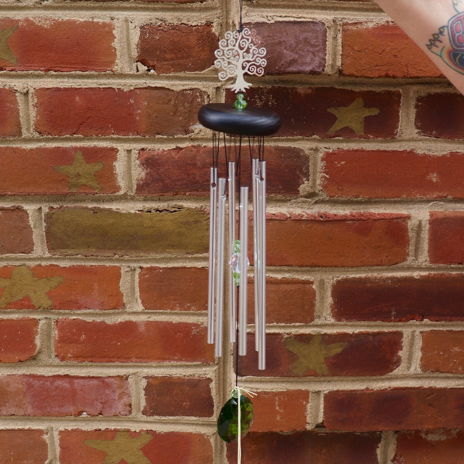 Someone holding up the Crystal Tree of Life Wind Chime in front of a brick wall.