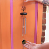 Someone holding up the Crystal Tree of Life Wind Chime in front of an orange and pink wall.