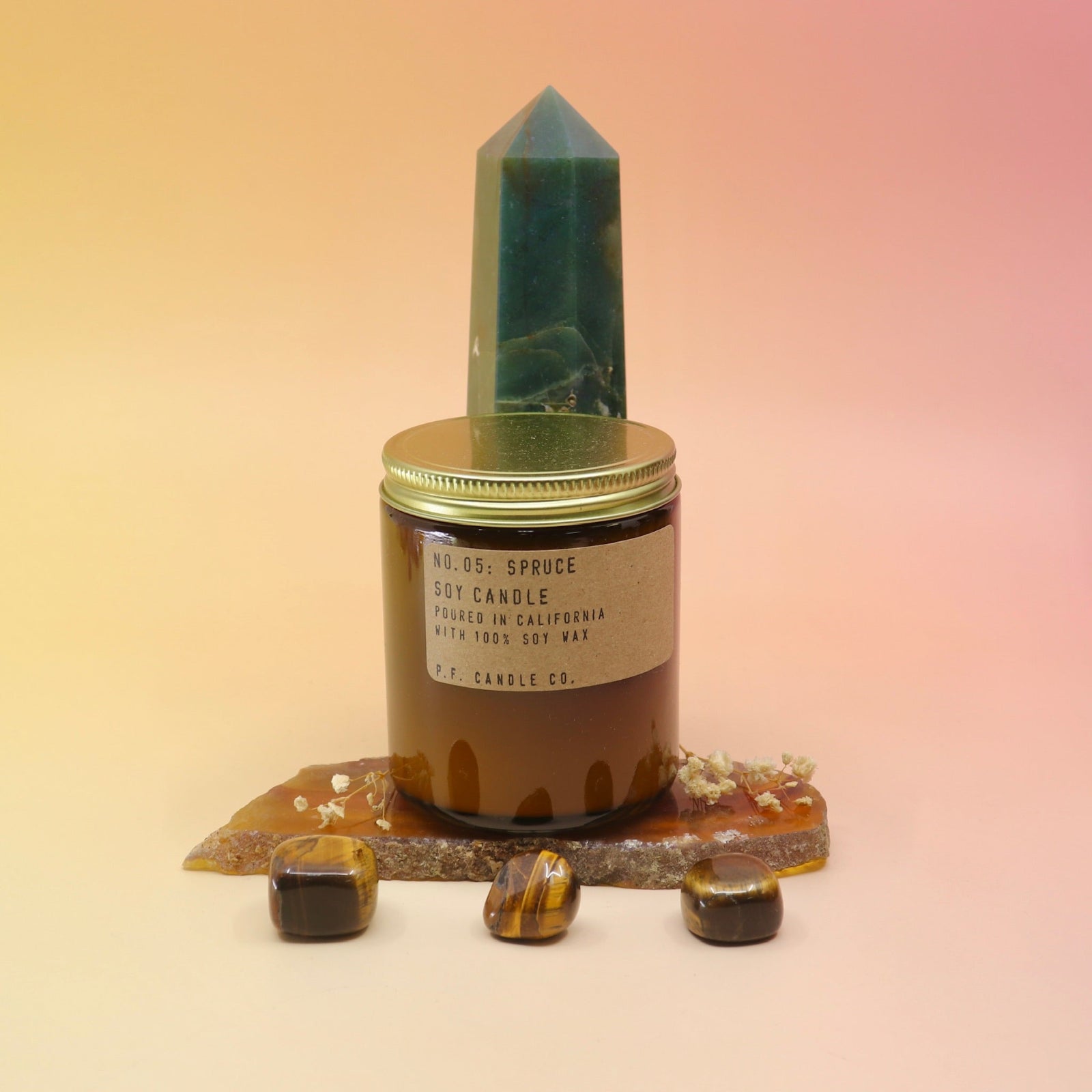 The Spruce Standard 7.2 oz Soy-Wax Candle on an agate slice and in front of a crystal tower all on a pink and yellow background.
