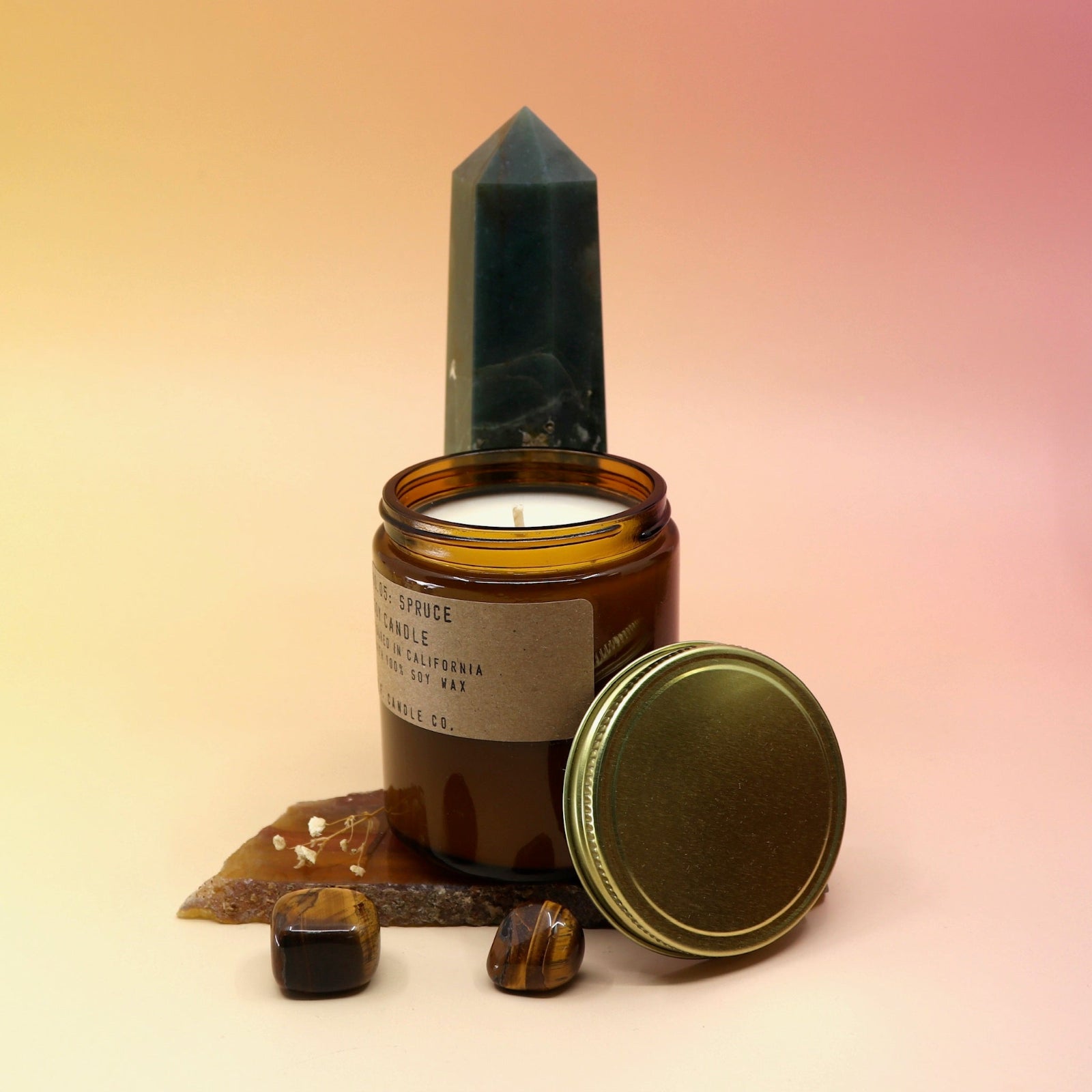 The Spruce Standard 7.2 oz Soy-Wax Candle on an agate slice and in front of a crystal tower all on a pink and yellow background.