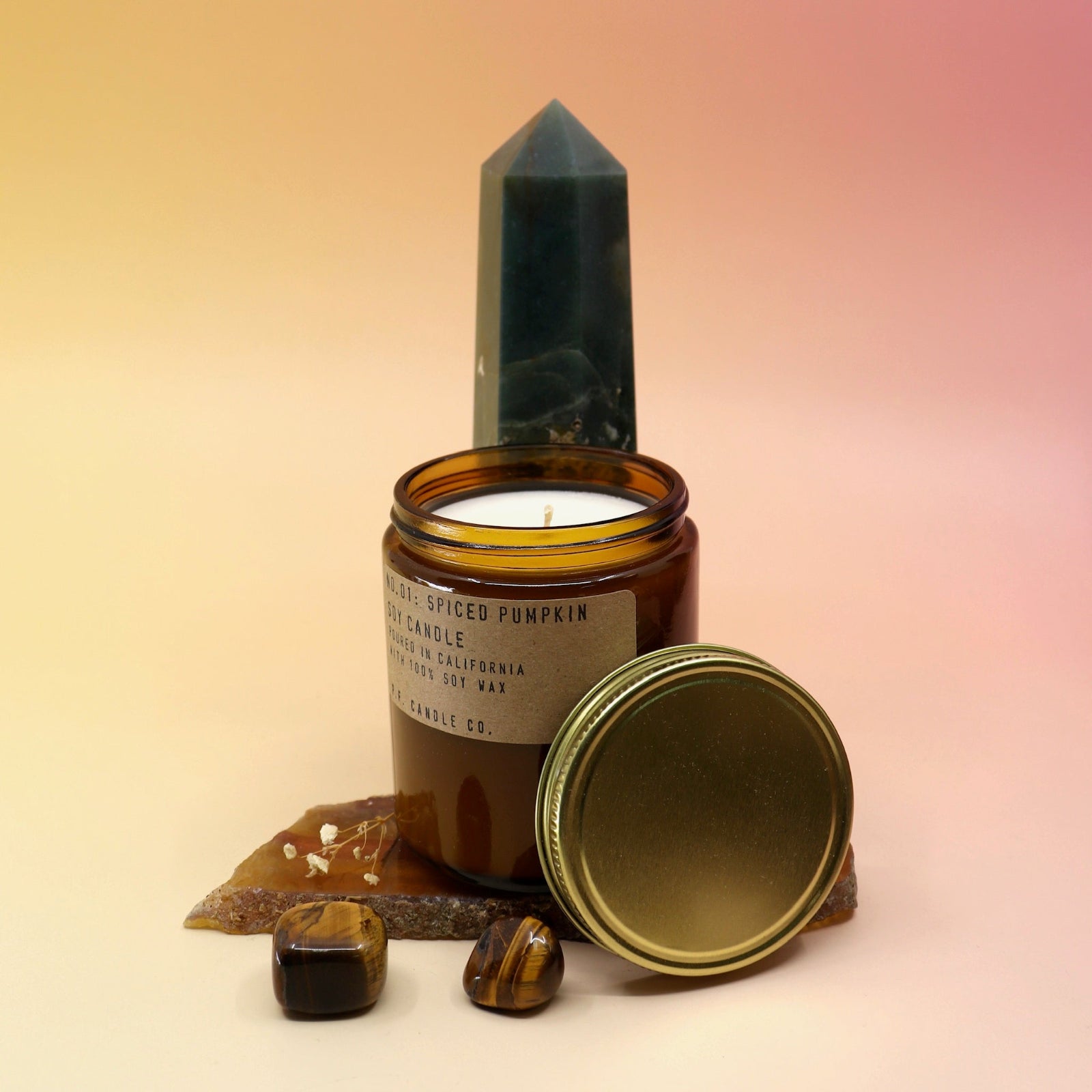 The Spiced Pumpkin Standard 7.2 oz Soy-Wax Candle on an agate slice and in front of a crystal tower all on a pink and yellow background.