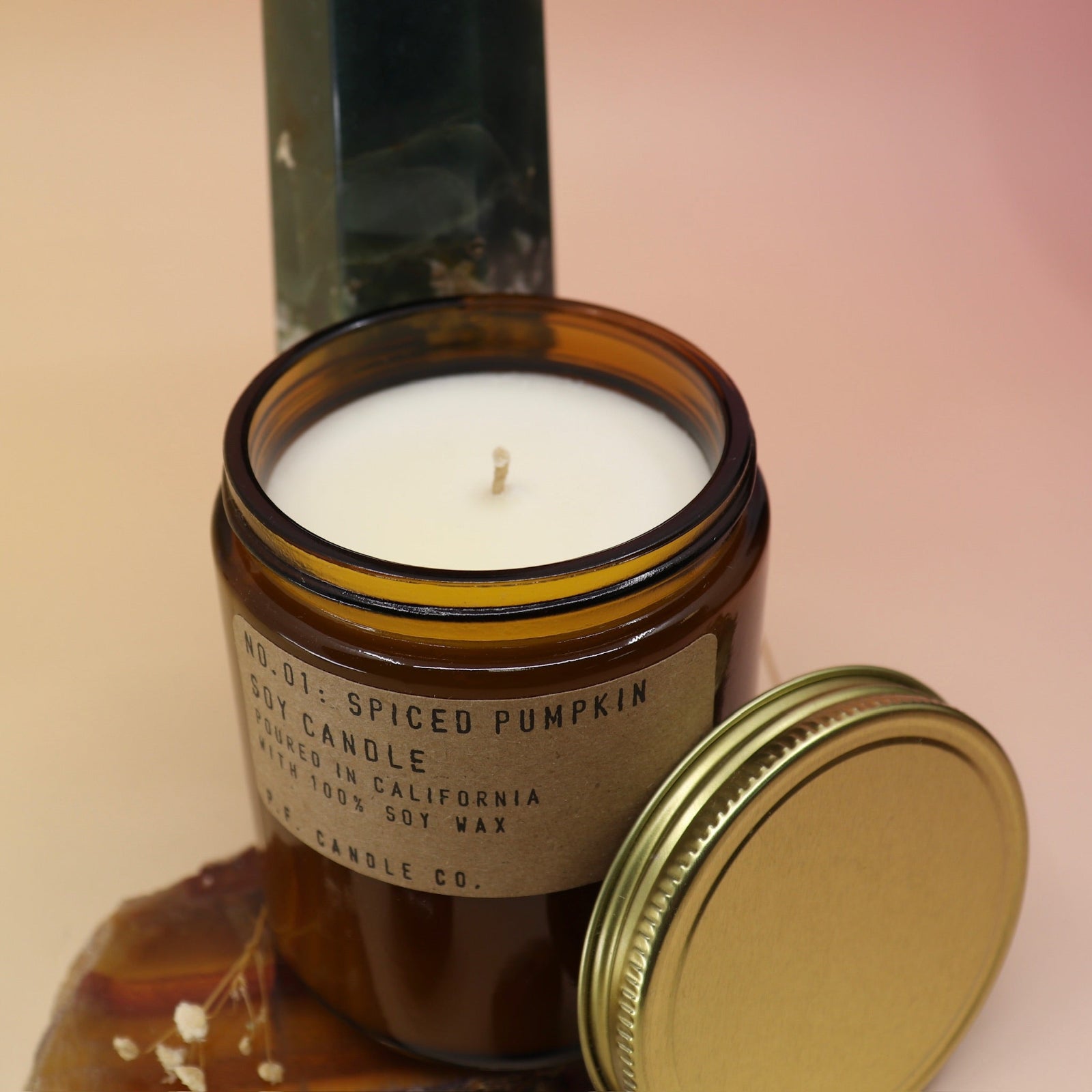 The Spiced Pumpkin Standard 7.2 oz Soy-Wax Candle on an agate slice and in front of a crystal tower all on a pink and yellow background.