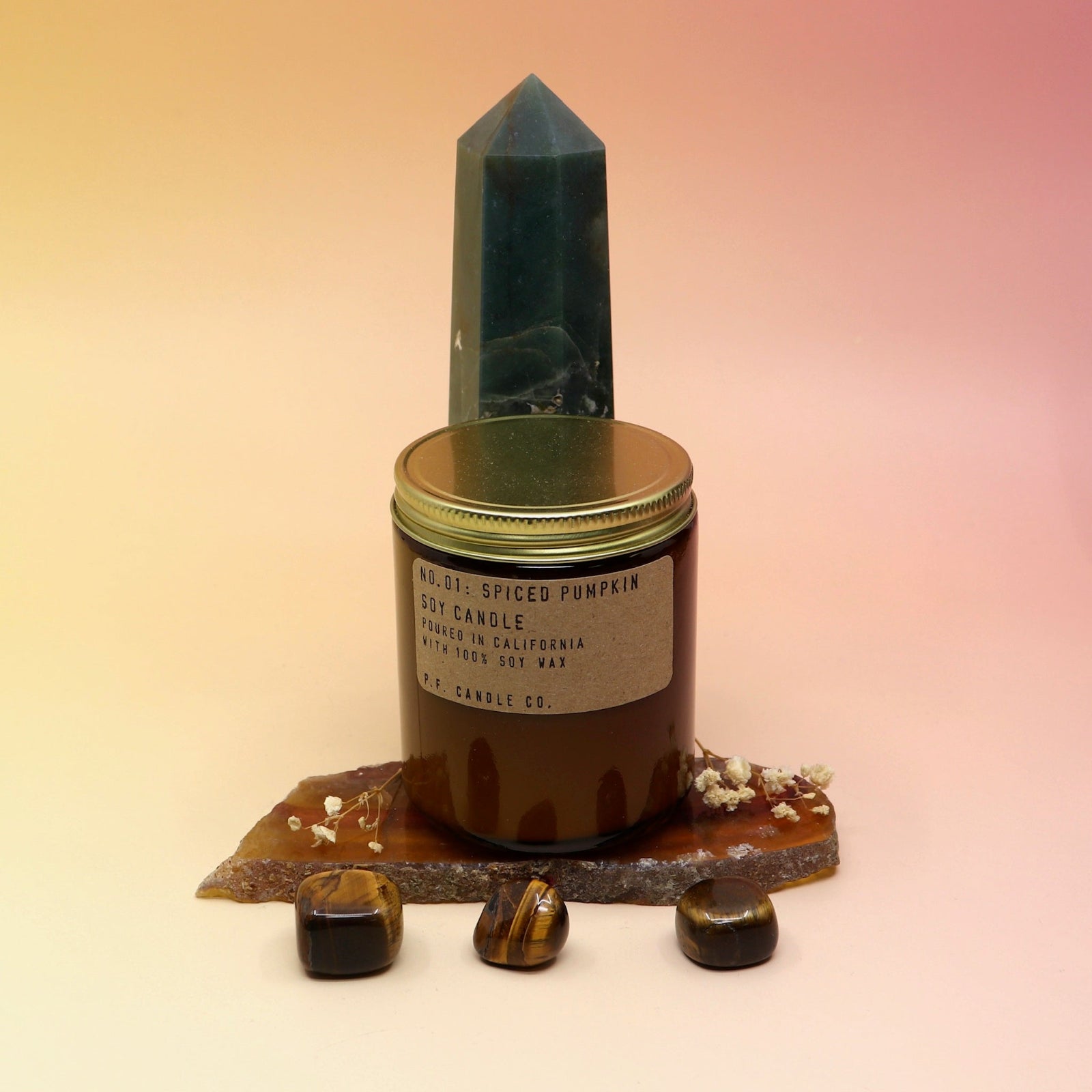 The Spiced Pumpkin Standard 7.2 oz Soy-Wax Candle on an agate slice and in front of a crystal tower all on a pink and yellow background.