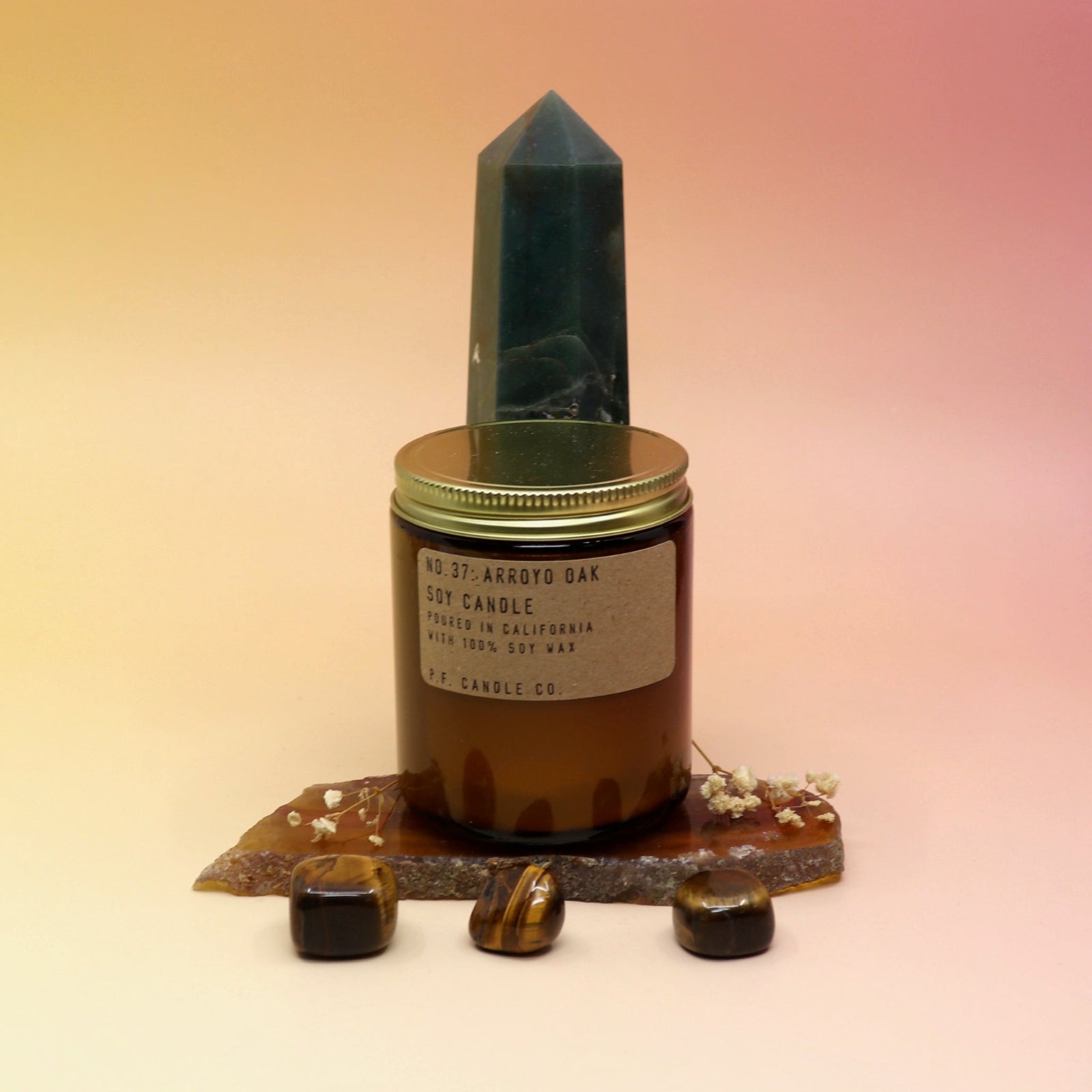 The Arroyo Oak Standard 7.2 oz Soy-Wax Candle on an agate slice and in front of a crystal tower all on a pink and yellow background.