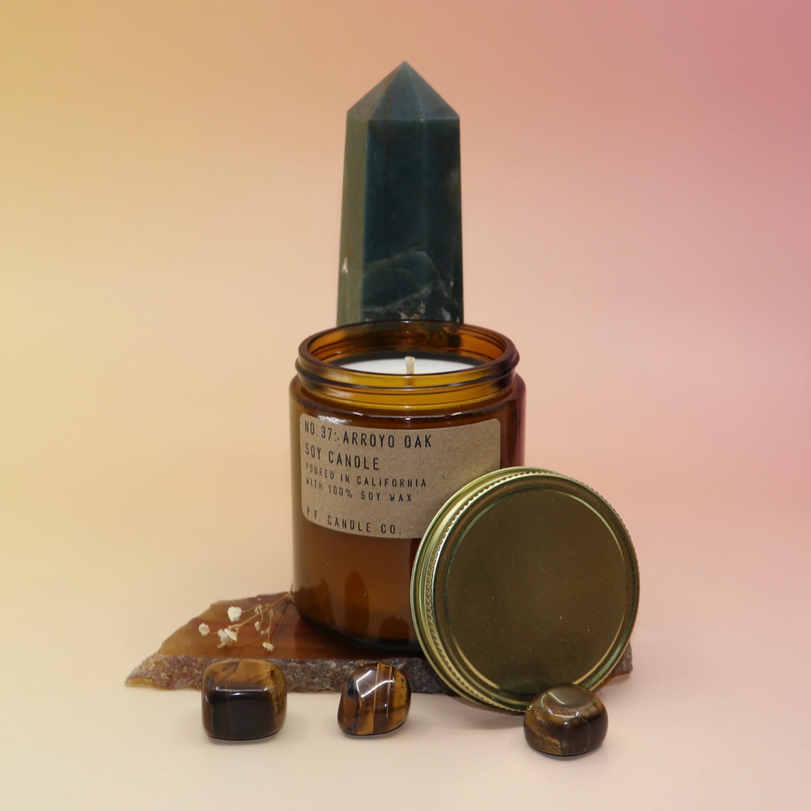 The Arroyo Oak Standard 7.2 oz Soy-Wax Candle on an agate slice and in front of a crystal tower all on a pink and yellow background.