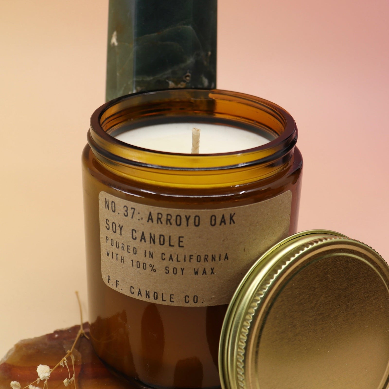 The Arroyo Oak Standard 7.2 oz Soy-Wax Candle on an agate slice and in front of a crystal tower all on a pink and yellow background.