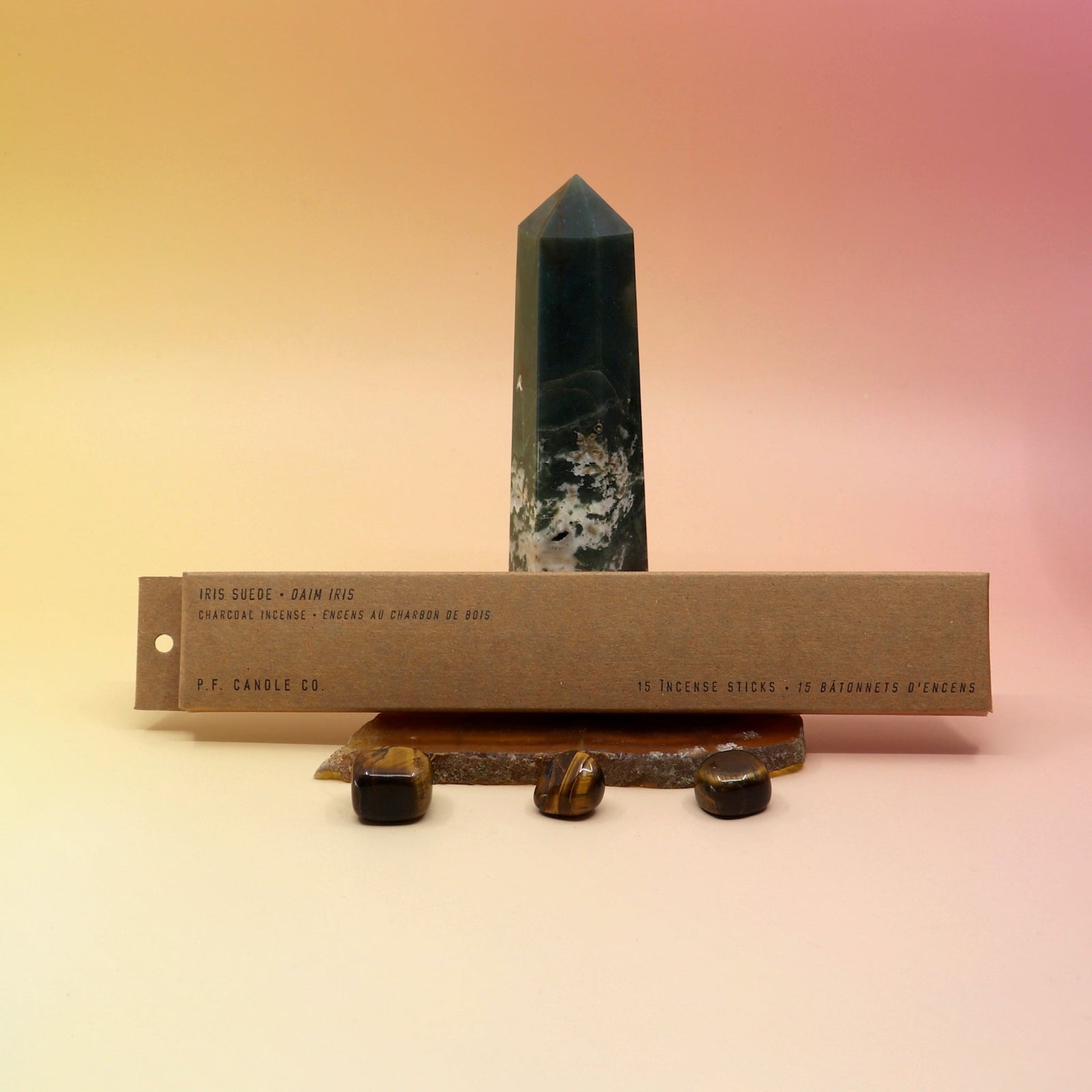 The P.F. Candle Co. Iris Suede Incense on an agate slice in front of a crystal tower all on a pink and yellow background.