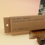 The P.F. Candle Co. Iris Suede Incense on an agate slice in front of a crystal tower all on a pink and yellow background.