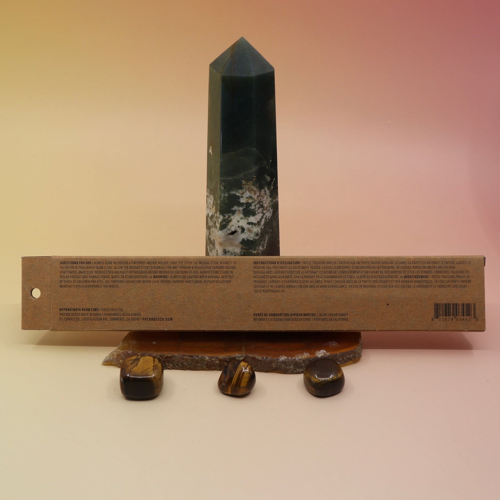 The back of the P.F. Candle Co. incense box on an agate slice all on a pink and yellow background.