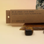 An up-close image of the P.F. Candle Co. Spruce Incense on an agate slice and in front of a crystal tower all on a pink and yellow background.