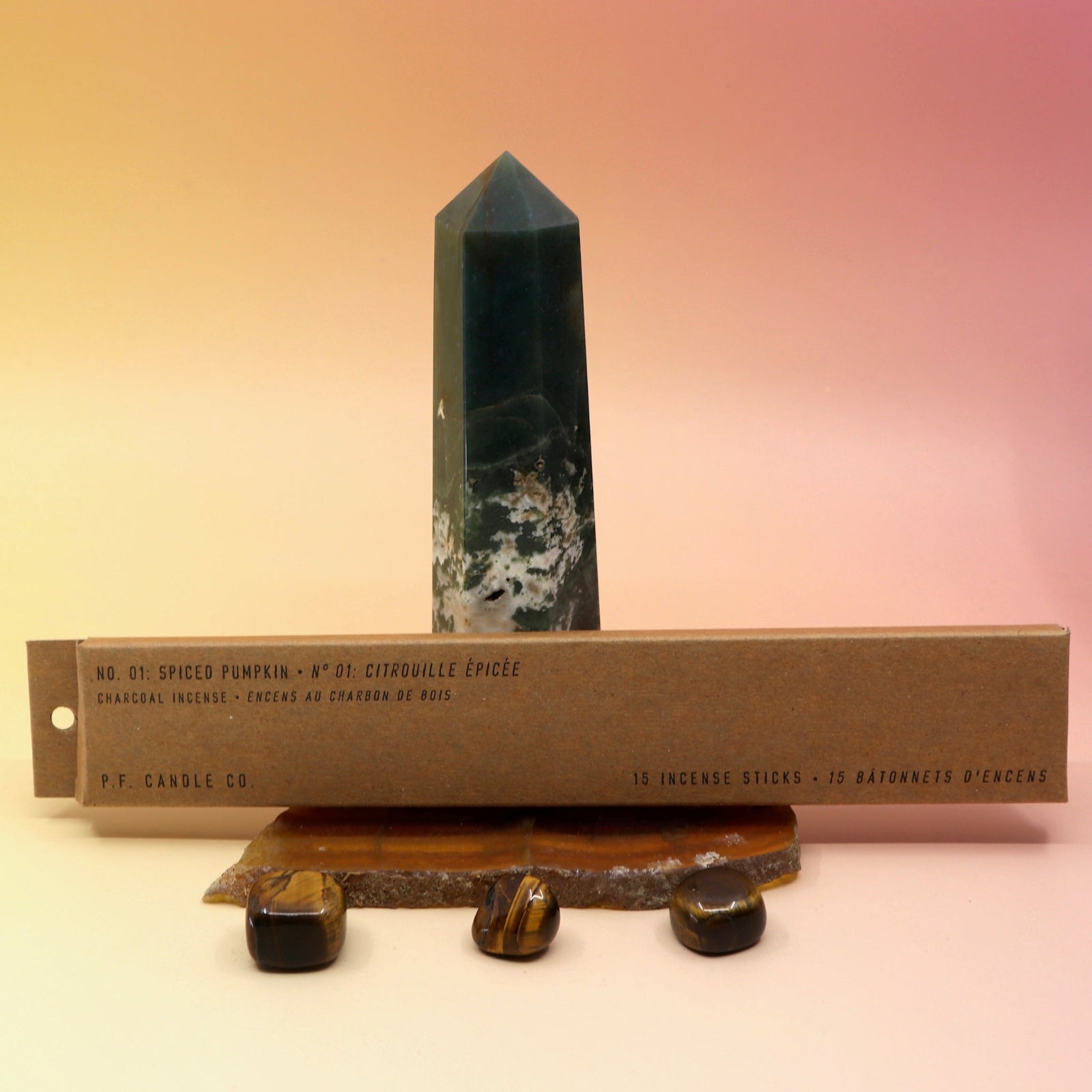 The P.F. Candle Co. Spiced Pumpkin Incense on an agate slice in front of a crystal tower, all on a pink and yellow background.