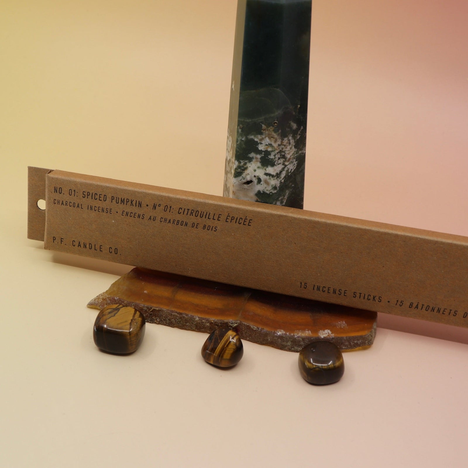 The P.F. Candle Co. Spiced Pumpkin Incense on an agate slice in front of a crystal tower, all on a pink and yellow background.