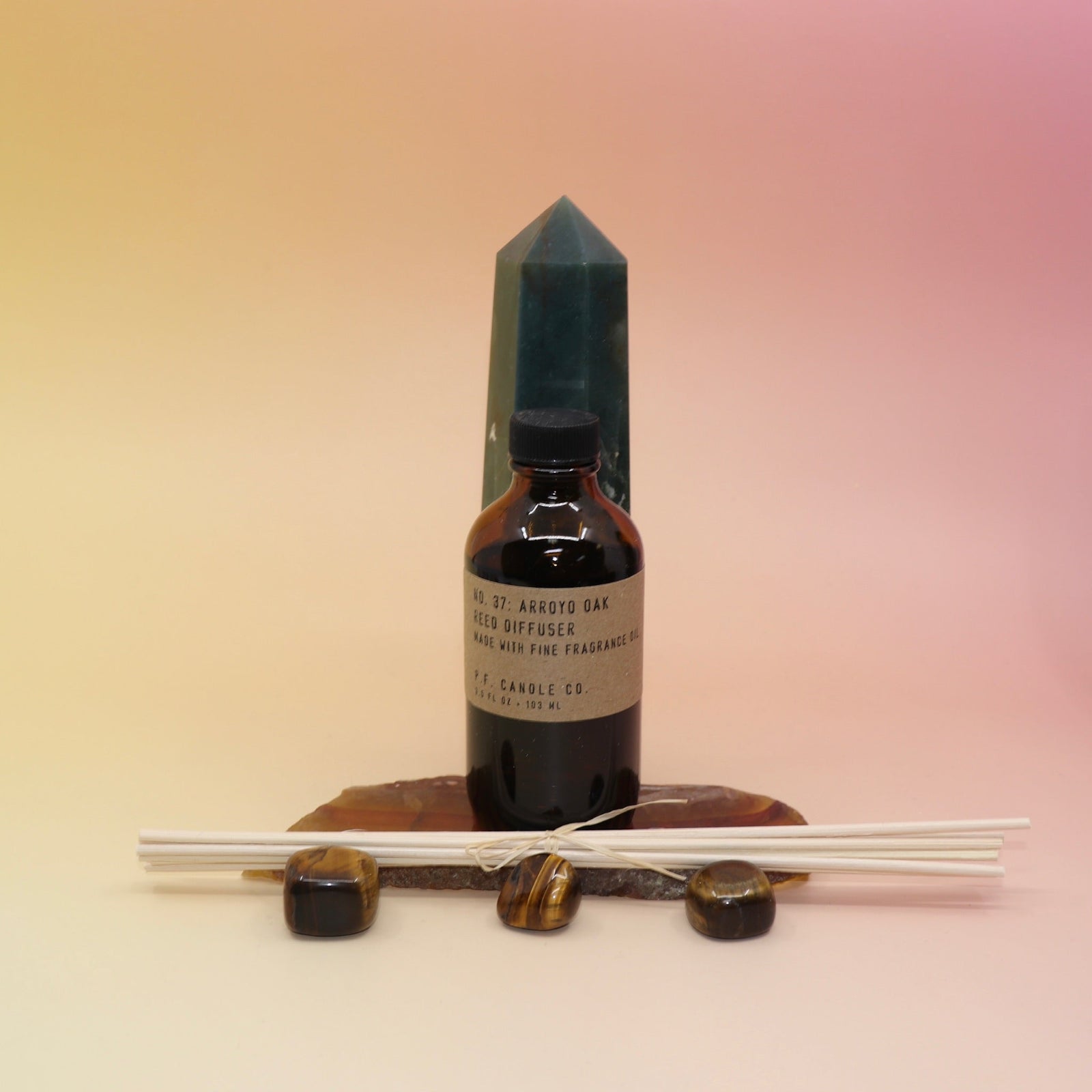 The P.F. Candle Co. Arroyo Oak - 3.5 oz Reed Diffuser on an agate slice and in front of a crystal tower all on a pink and yellow background.