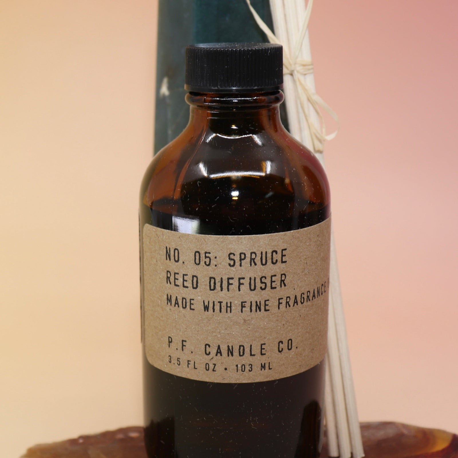 An up-close image of the P.F. Candle Co. Spruce - 3.5 oz Reed Diffuser on an agate slice in front of a crystal tower.