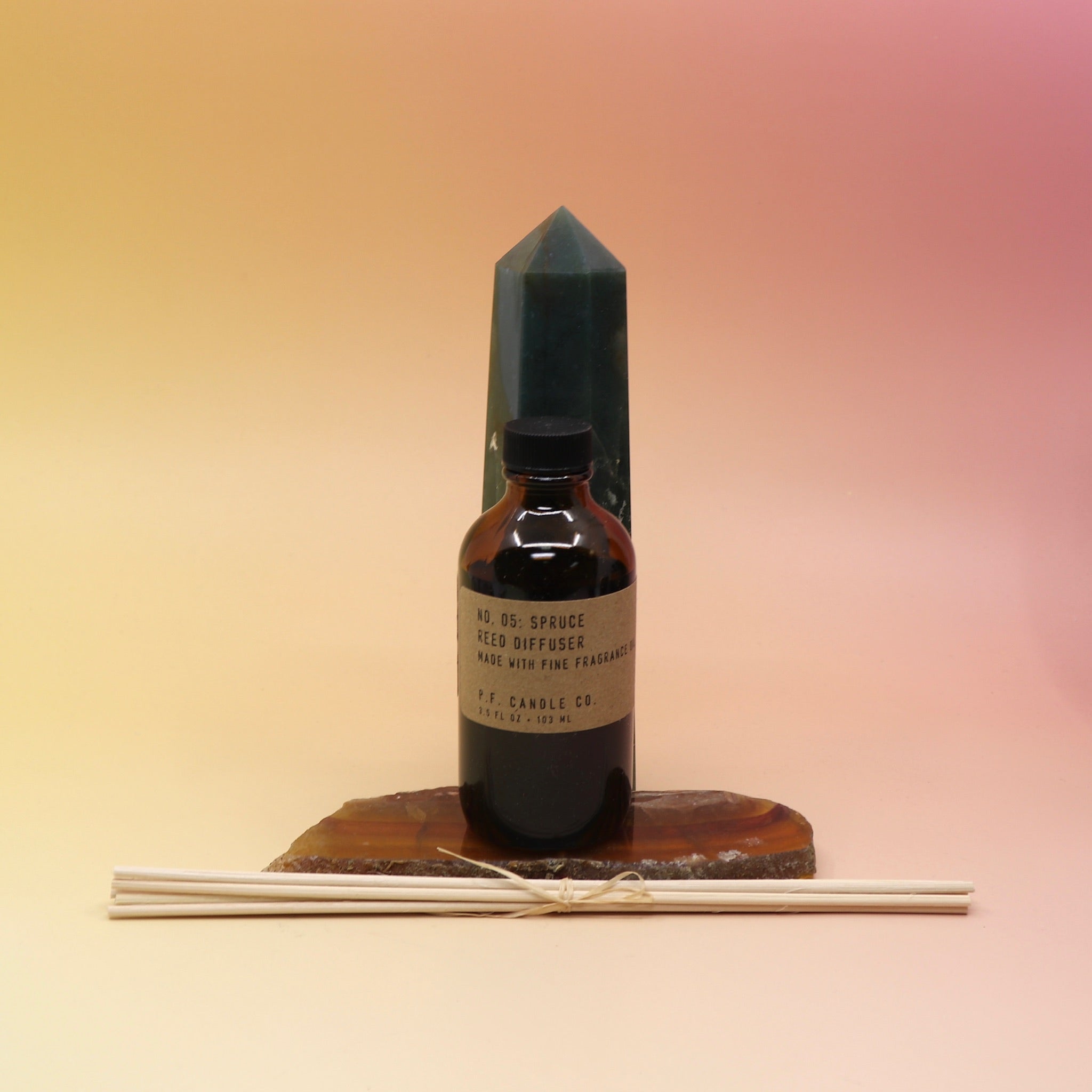 The P.F. Candle Co. Spruce - 3.5 oz Reed Diffuser on an agate slice in front of a crystal tower.