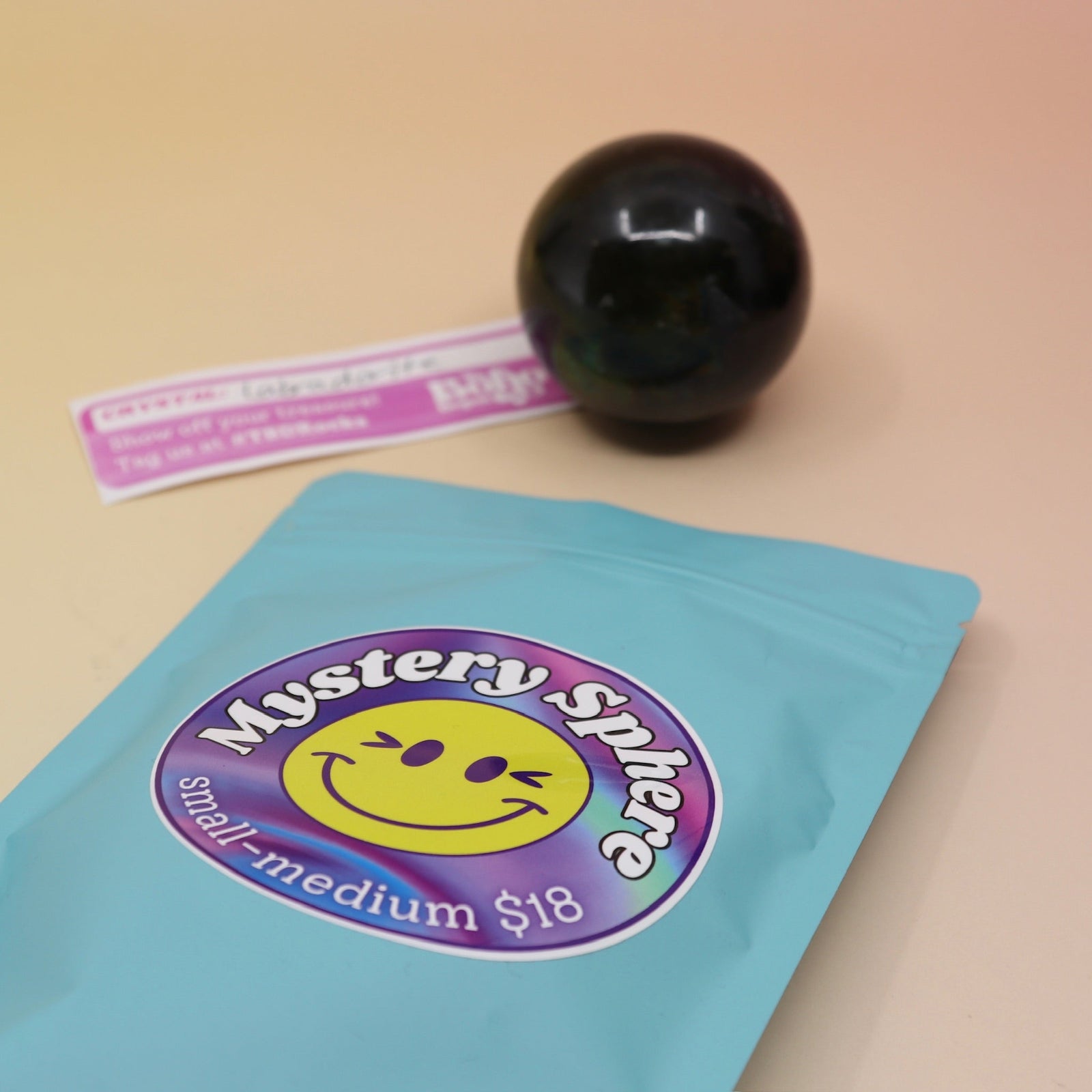 A small - medium Mystery Crystal Sphere Bag open with its contents on a pink and yellow background.