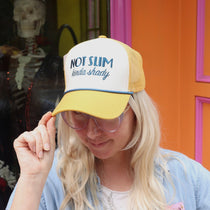 A woman wearing the Not Slim Kinda Shady Trucker Hat in front of a pink and orange wall.