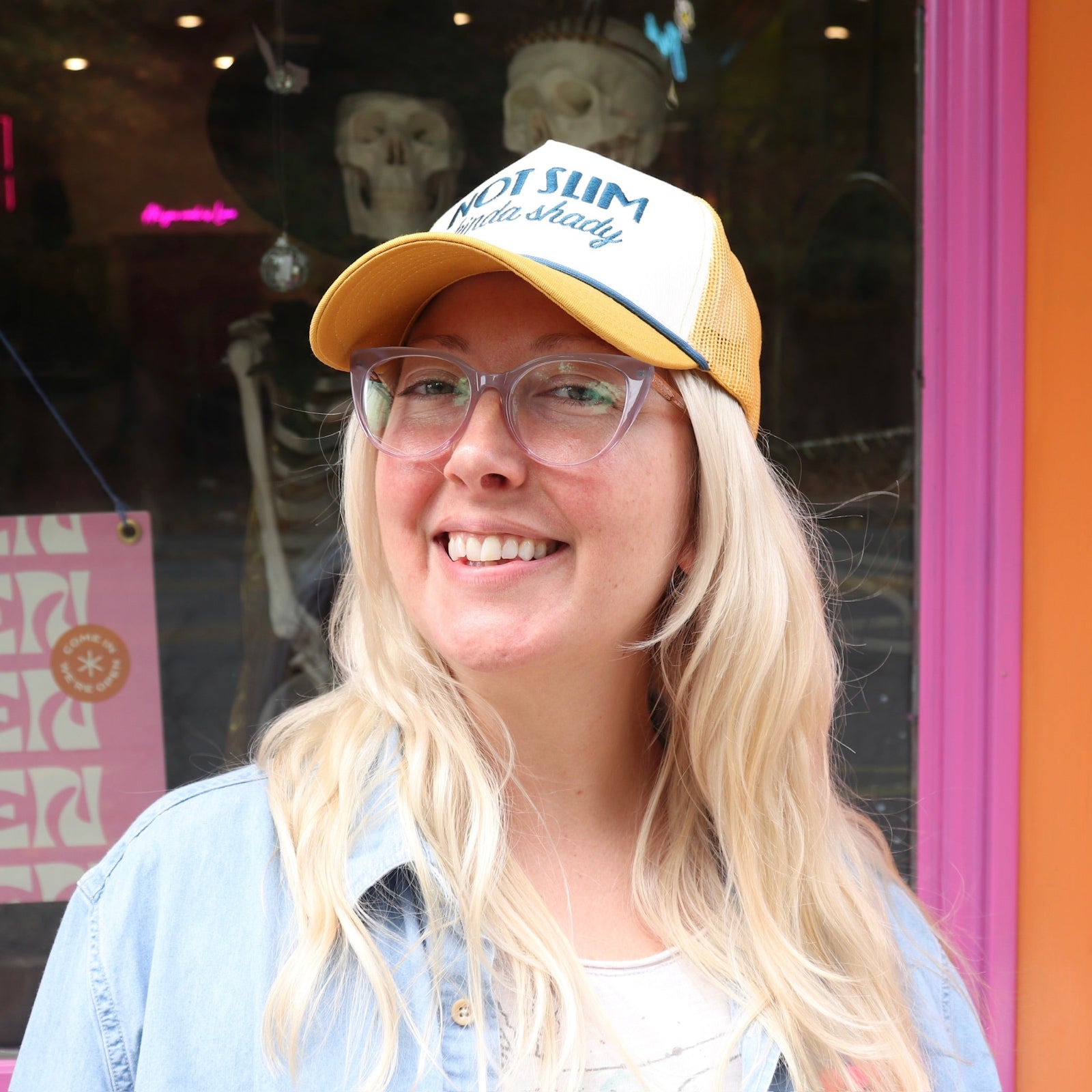 A woman wearing the Not Slim Kinda Shady Trucker Hat in front of a window and a pink and orange wall.
