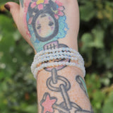 Someone wearing four Opalite Crystal Bracelets on their wrist in front of a green nature background.