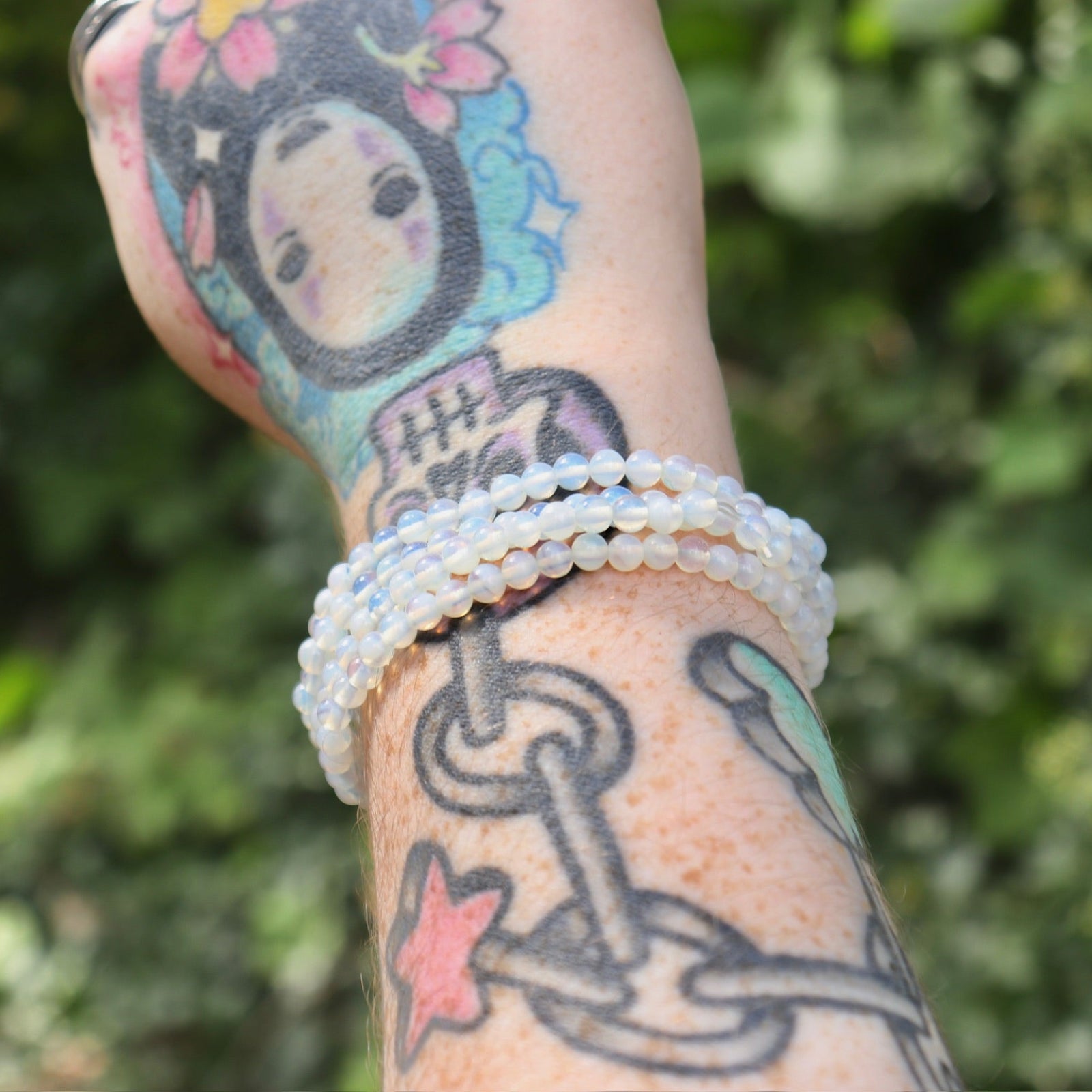 Someone wearing three Opalite Crystal Bracelets on their wrist in front of a green nature background.