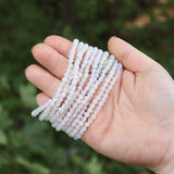 Someone holding multiple Opalite Crystal Bracelets in their hand in front of a green nature background.