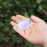 Someone holding the Opalite Worry Stone in front of some greenery.
