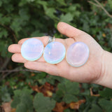 Someone holding three Opalite Worry Stones in front of some greenery.