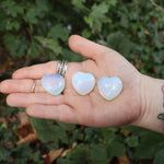 Someone holding three Opalite Crystal Hearts in front of a green outside background.