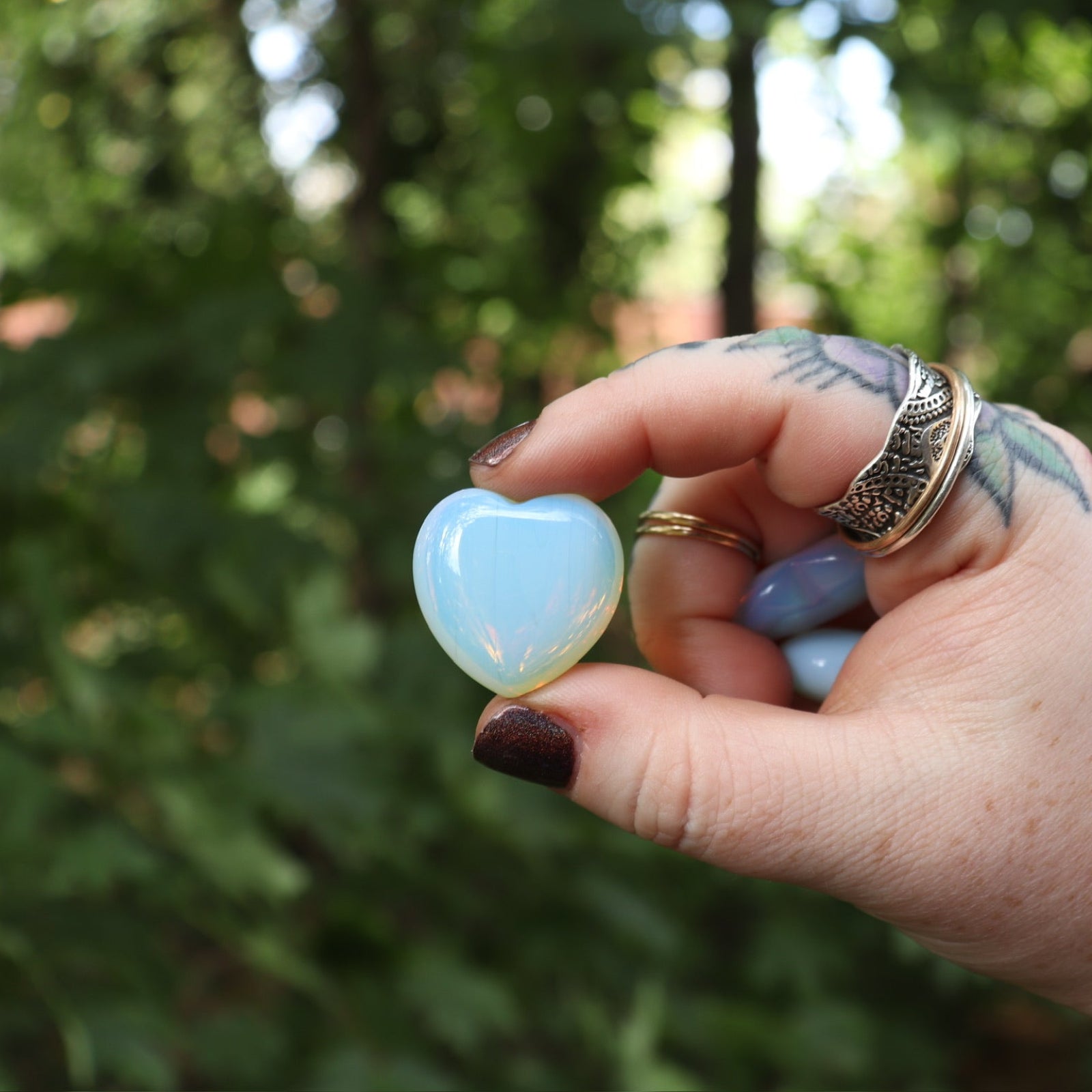 Someone holding the Opalite Crystal Heart in front of a green outside background.